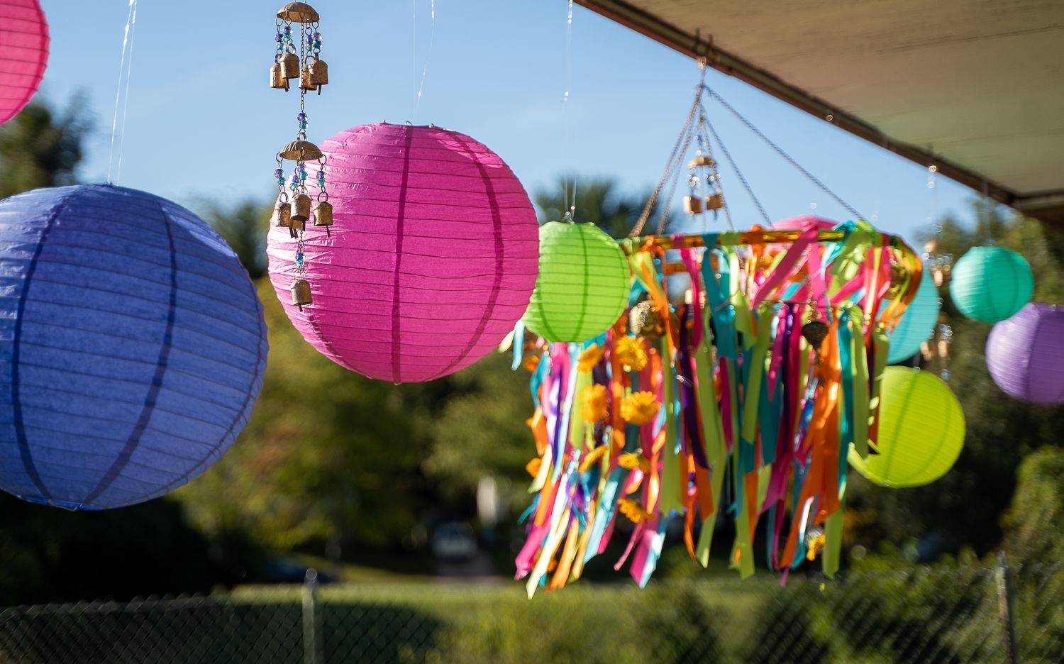 Colorful paper lanterns and ribbon decorations hanging outdoors under a canopy.