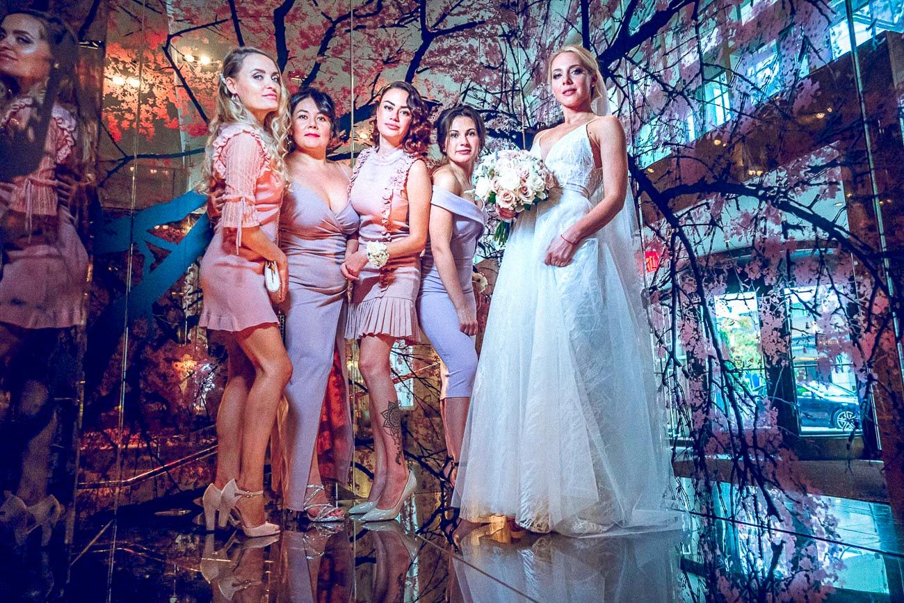 Bride holding bouquet stands with four bridesmaids in pink dresses in decorated wedding venue.