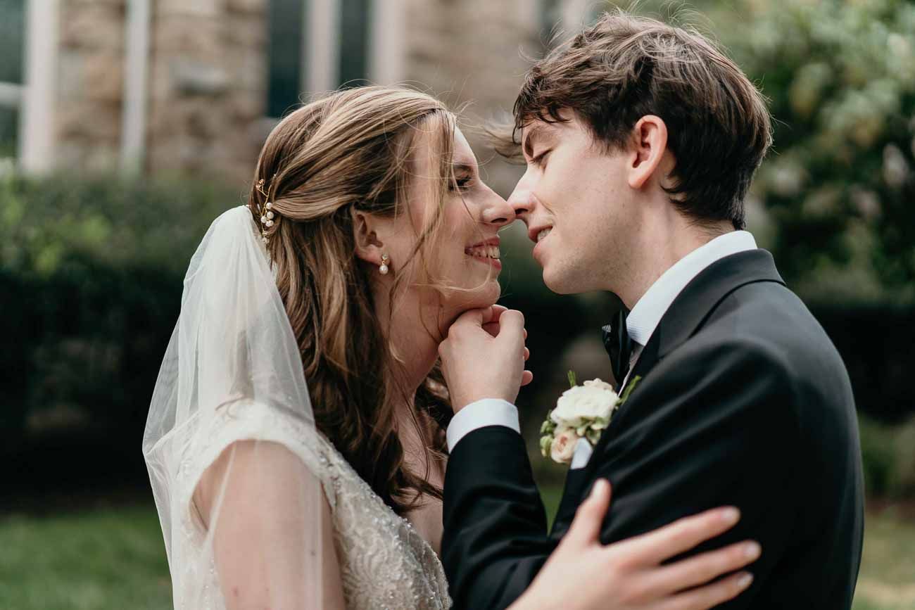 Bride and groom share an intimate moment, nearly kissing outdoors on their wedding day.
