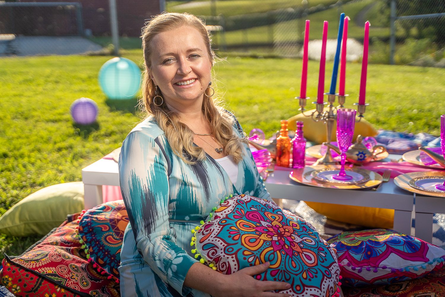 Woman in teal dress holding a colorful pillow at a vibrant outdoor table.