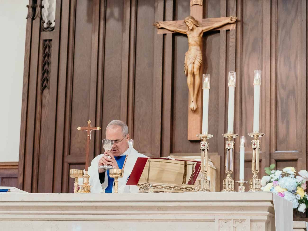 Catholic priest performs wedding Mass at wooden altar with crucifix and lit candles.
