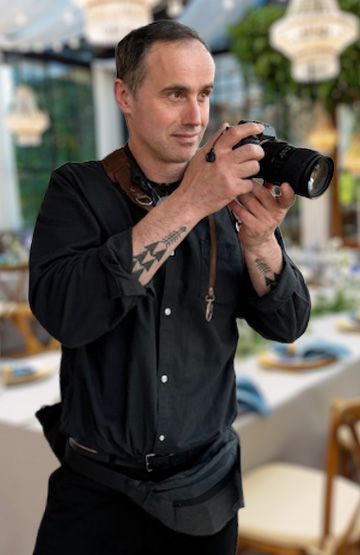 Tattooed wedding photographer holding a DSLR camera at an elegant venue.