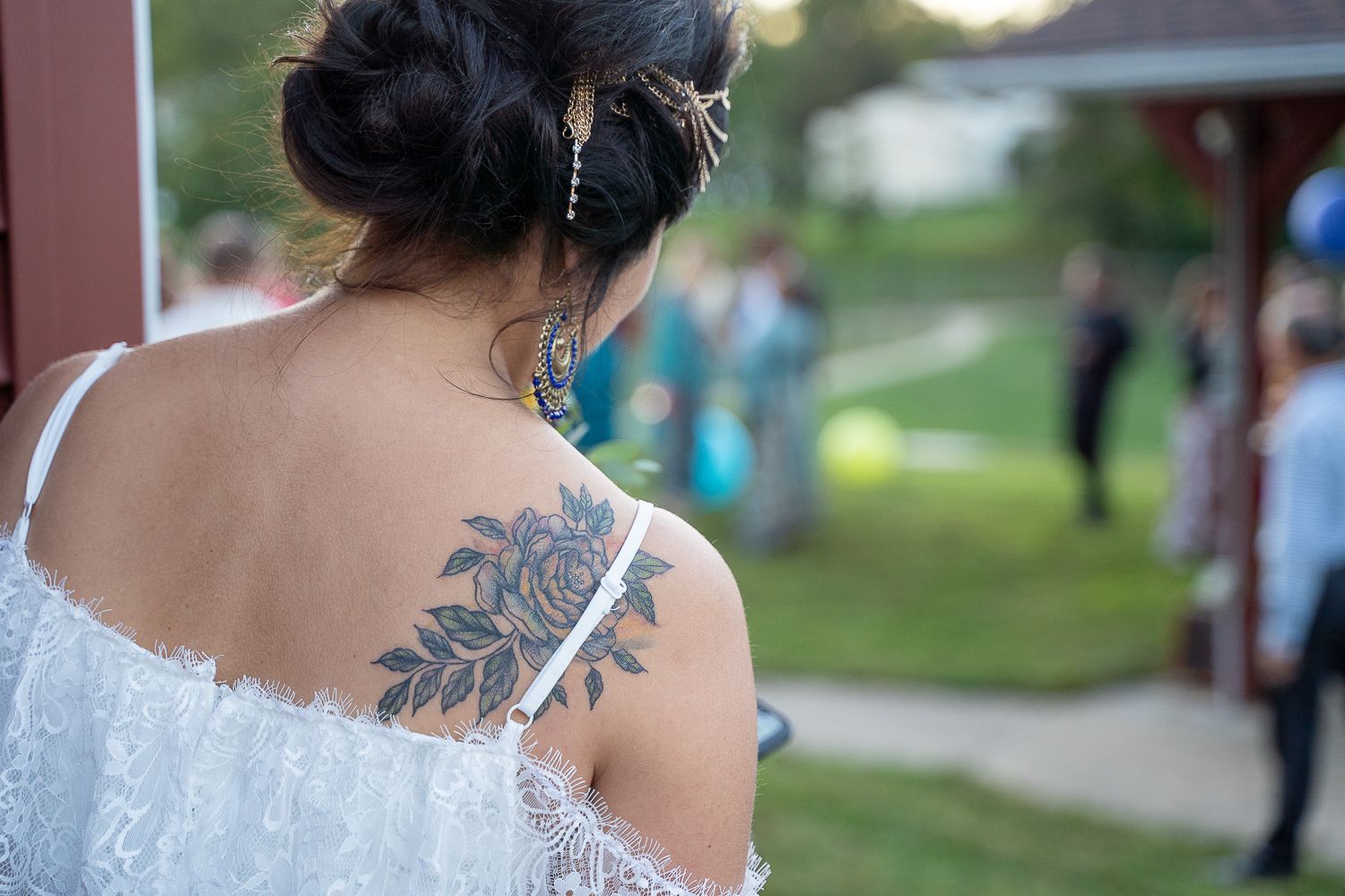 Close-up of floral tattoo on womans upper back at an outdoor wedding celebration.