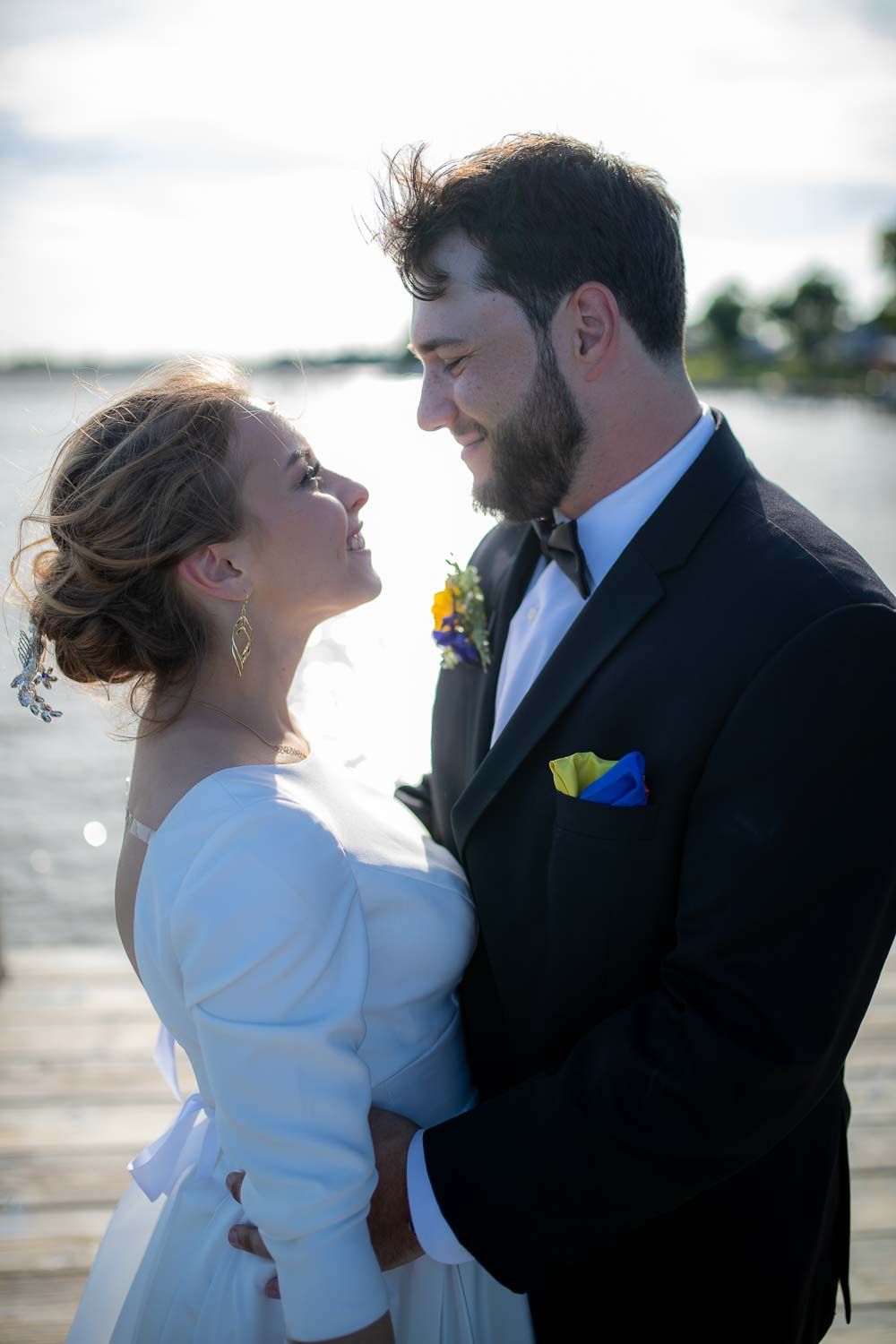 Bride and groom gazing lovingly at each other on waterfront dock at golden hour.