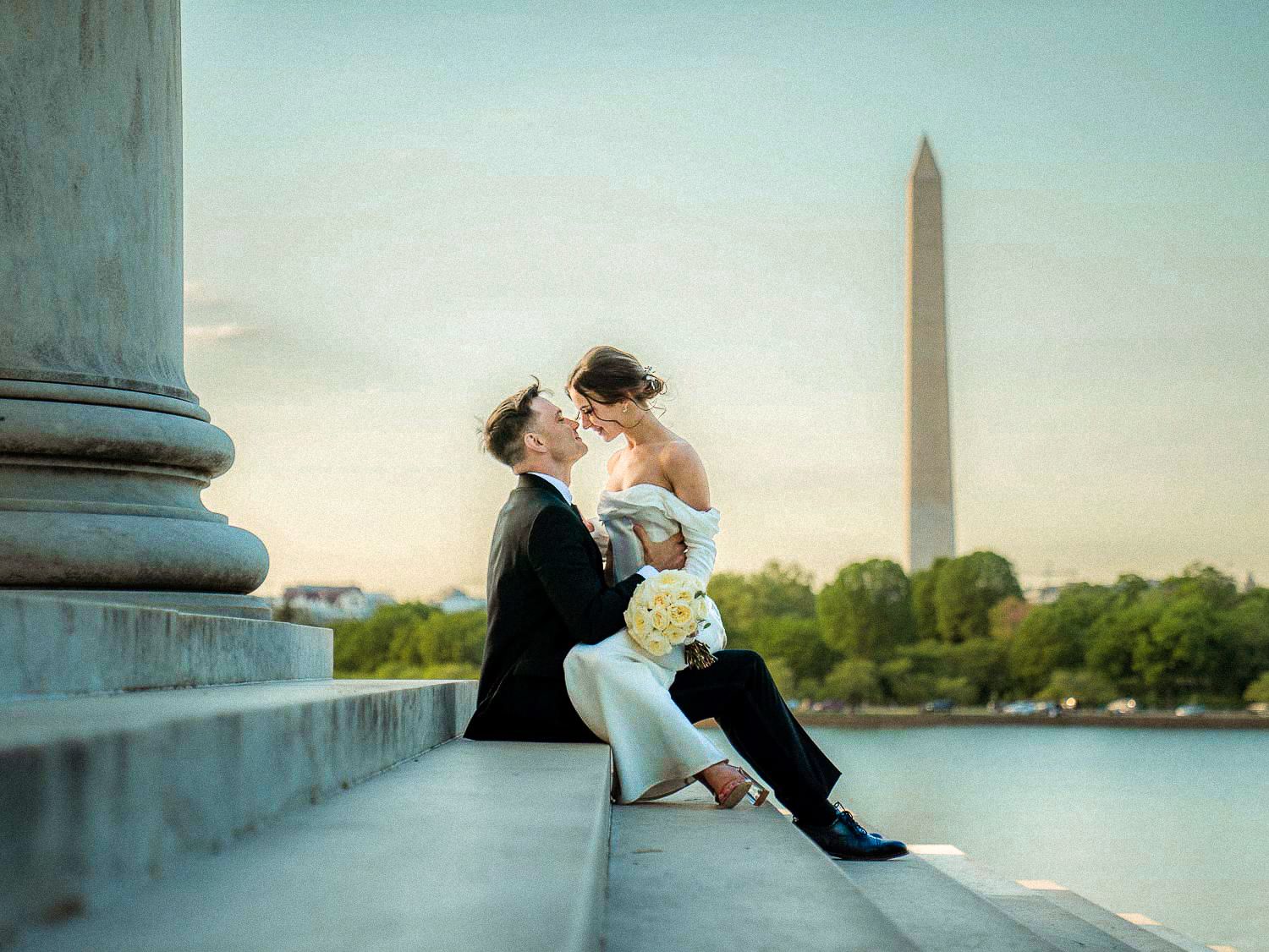 Bride and groom sit on steps near the Washington Monument at sunset, sharing a tender kiss.