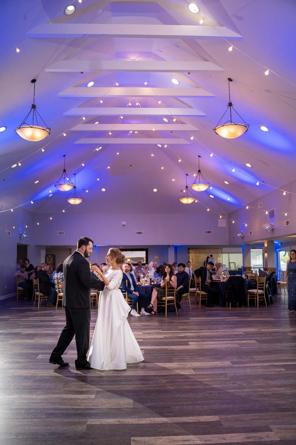 Bride and groom dancing alone on dance floor in stunning blue-lit wedding reception hall.