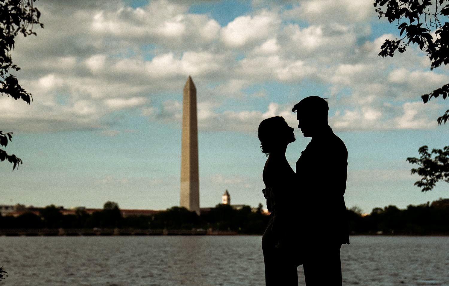 Silhouette of couple facing each other with Washington Monument and Tidal Basin at sunset behind them.