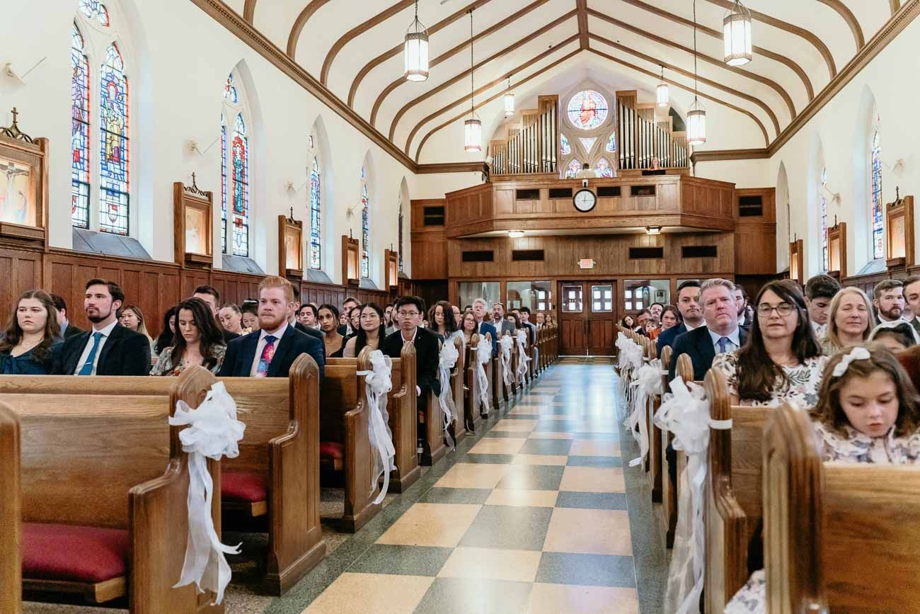 Full church congregation seated in wooden pews during a wedding ceremony with stained glass windows and pipe organ.