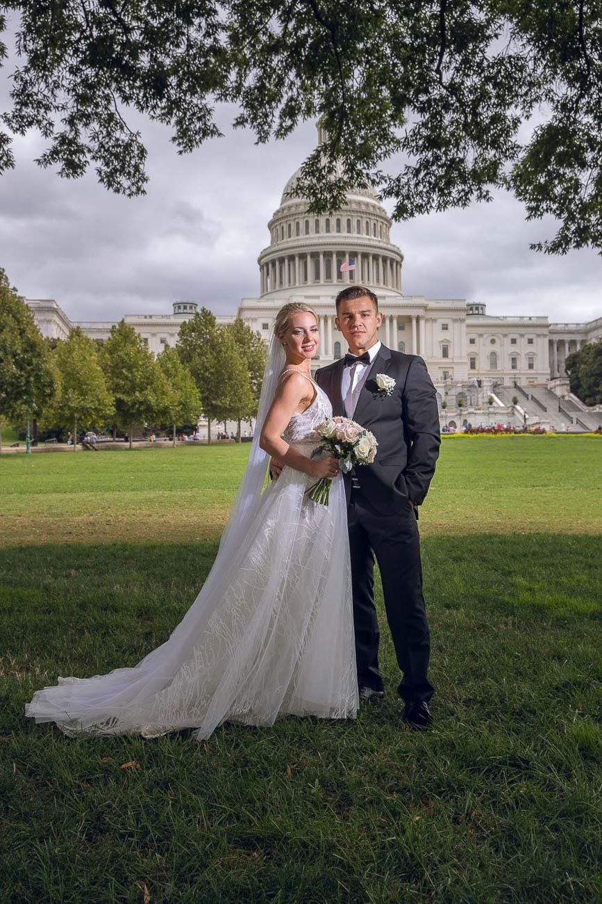 Wedding couple posing under a tree with the iconic US Capitol dome in the background.