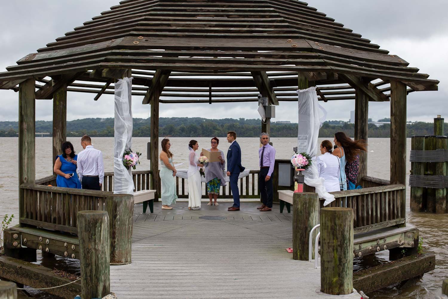 Small intimate wedding ceremony held under a wooden gazebo on a dock overlooking a serene river.