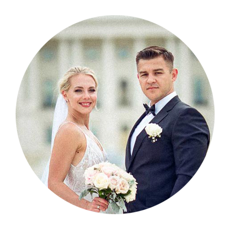 Elegant bride holding bouquet and groom in tuxedo posing in front of a grand white building.