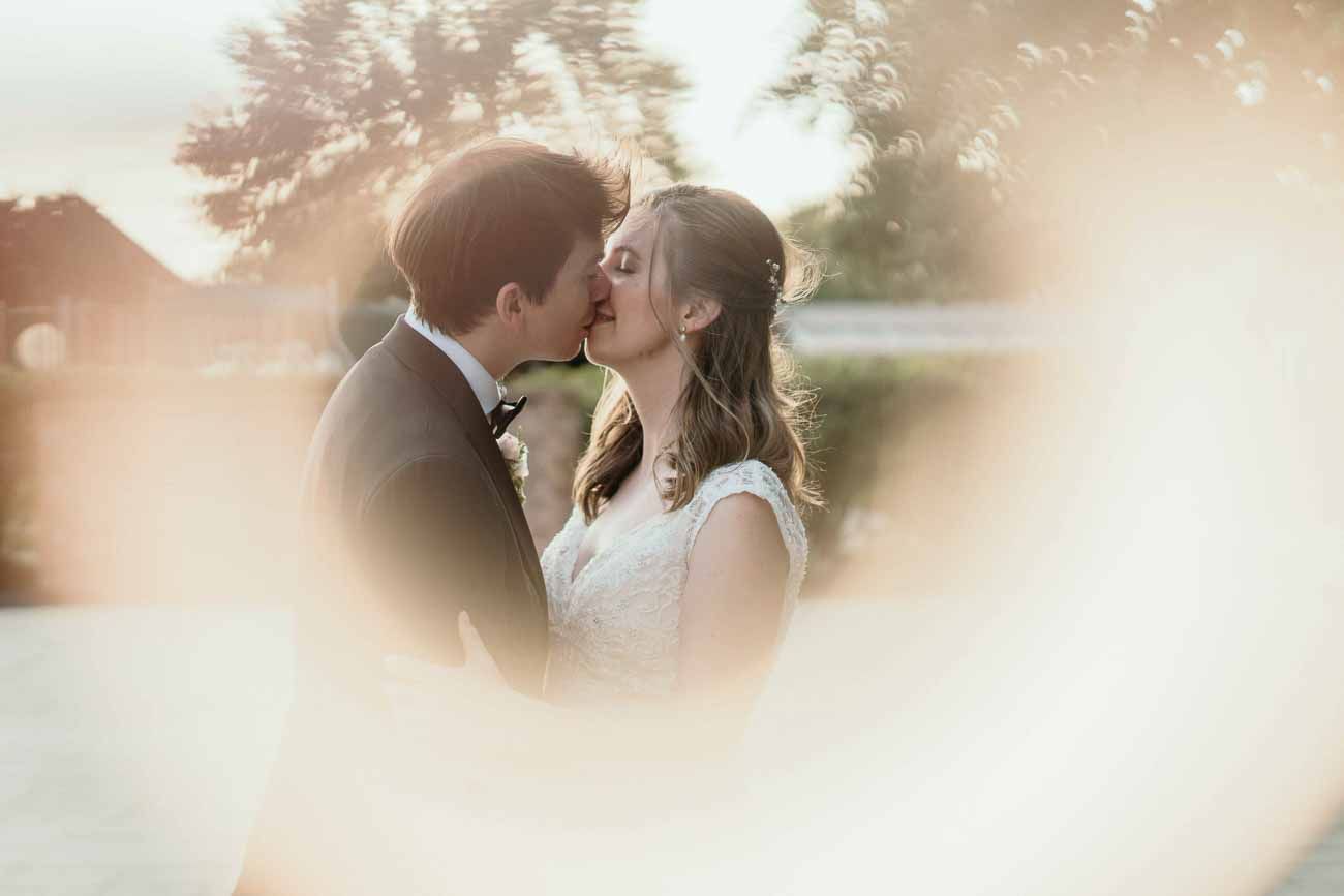 Bride and groom sharing a romantic kiss bathed in warm golden sunlight on their wedding day.