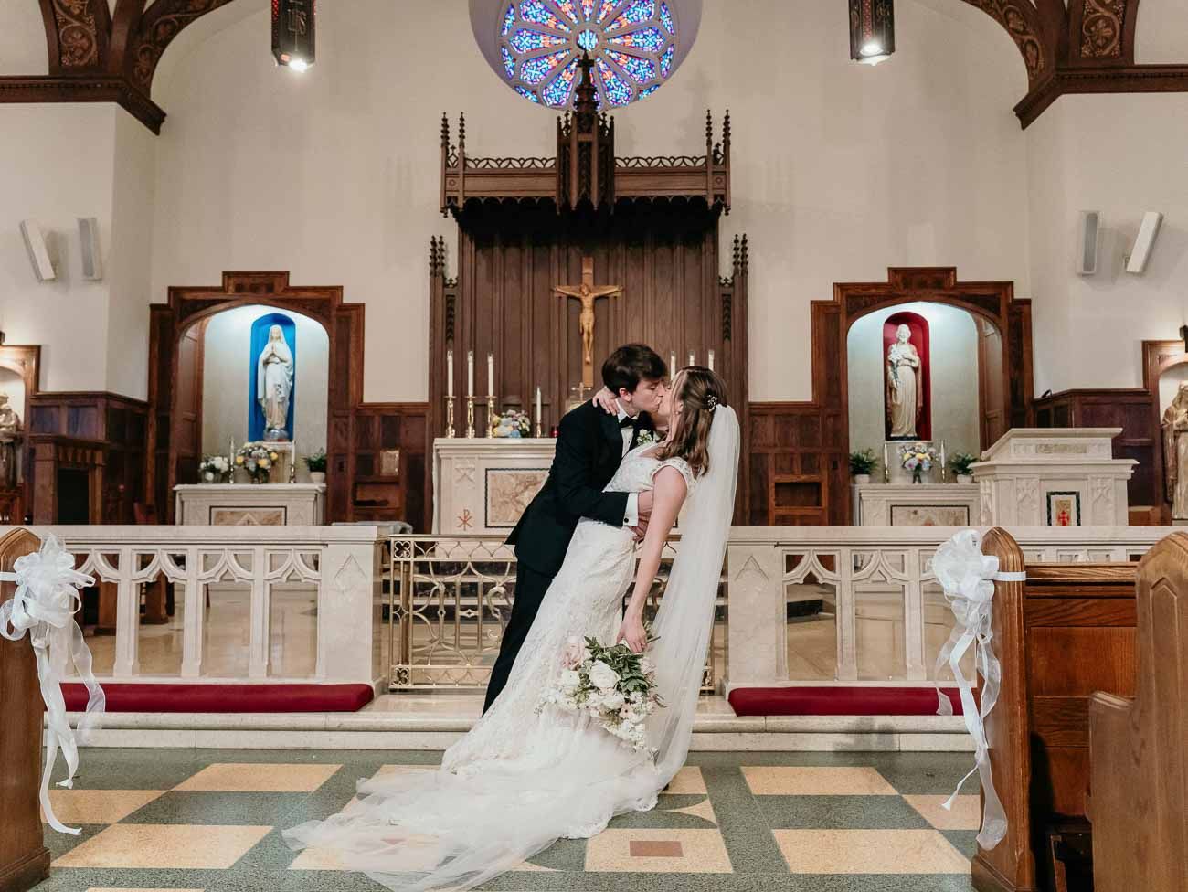 Bride and groom share romantic dip kiss at Catholic church altar after their wedding ceremony.