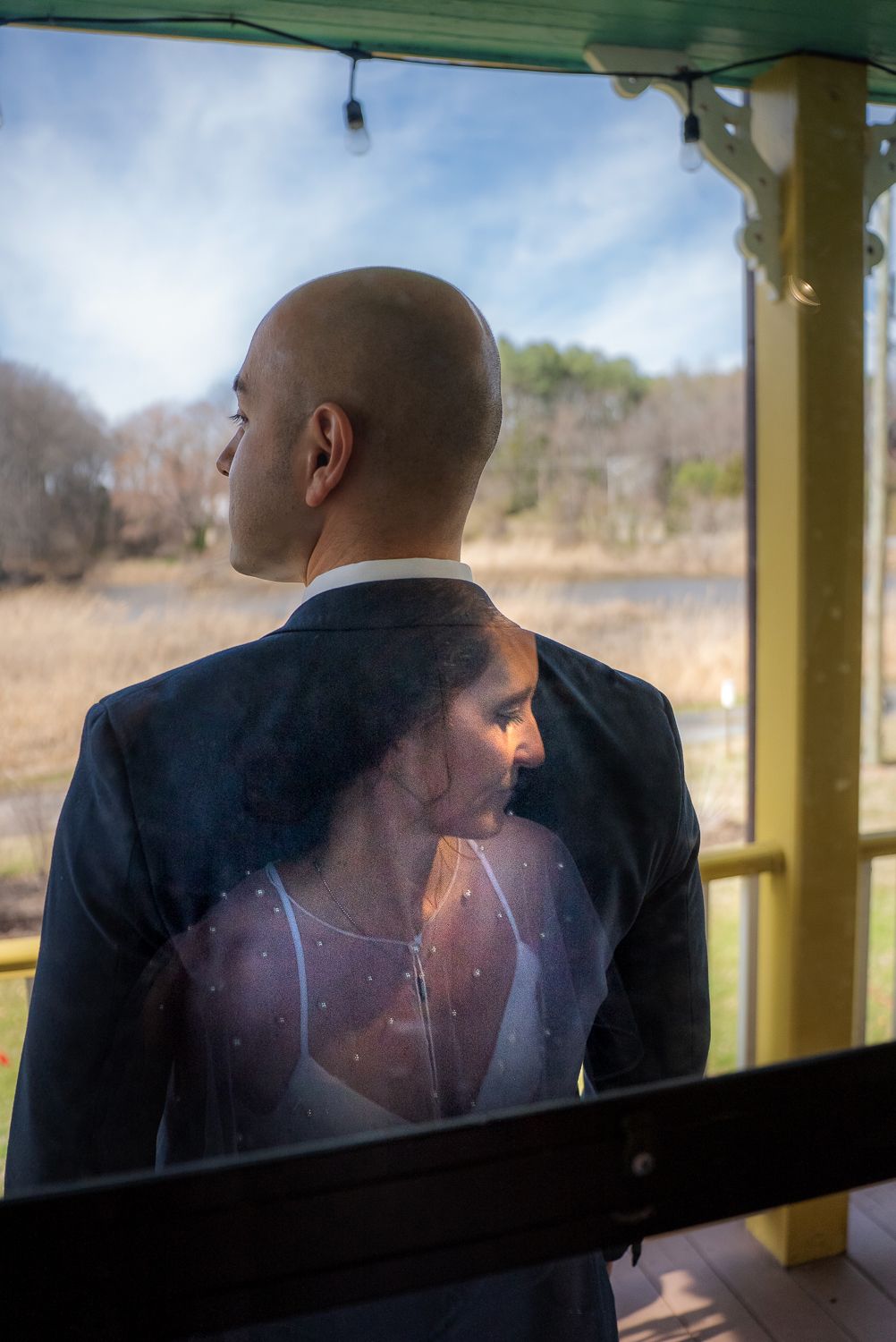 Bride and groom reflected in glass window overlooking scenic outdoor landscape on wedding day.