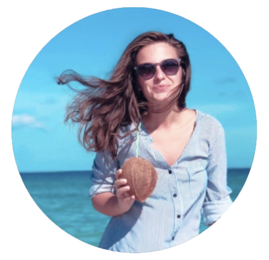 Happy woman in sunglasses holding a coconut on a sunny beach with turquoise ocean water.
