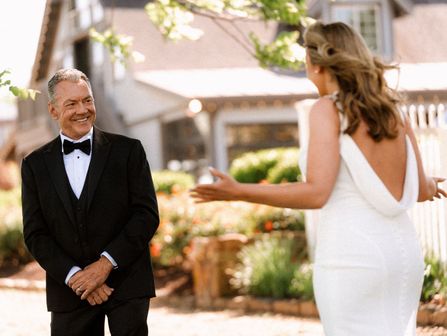 Father smiles emotionally seeing bride in white wedding dress during outdoor first look ceremony.
