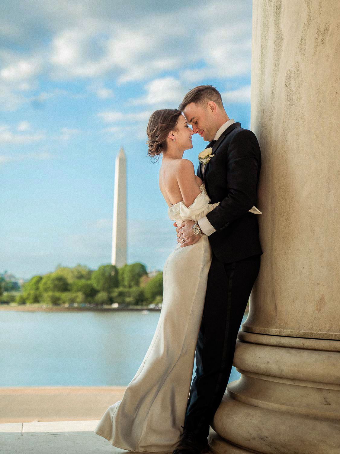 Bride and groom touch foreheads tenderly beside a marble column with the Washington Monument view.