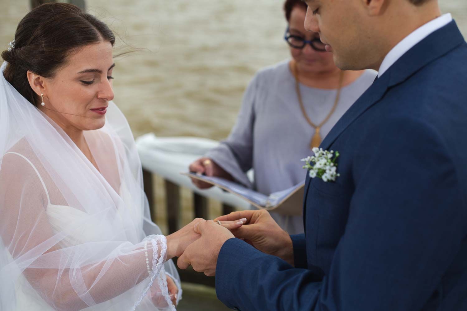 Groom places wedding ring on brides finger during emotional outdoor ceremony with officiant.