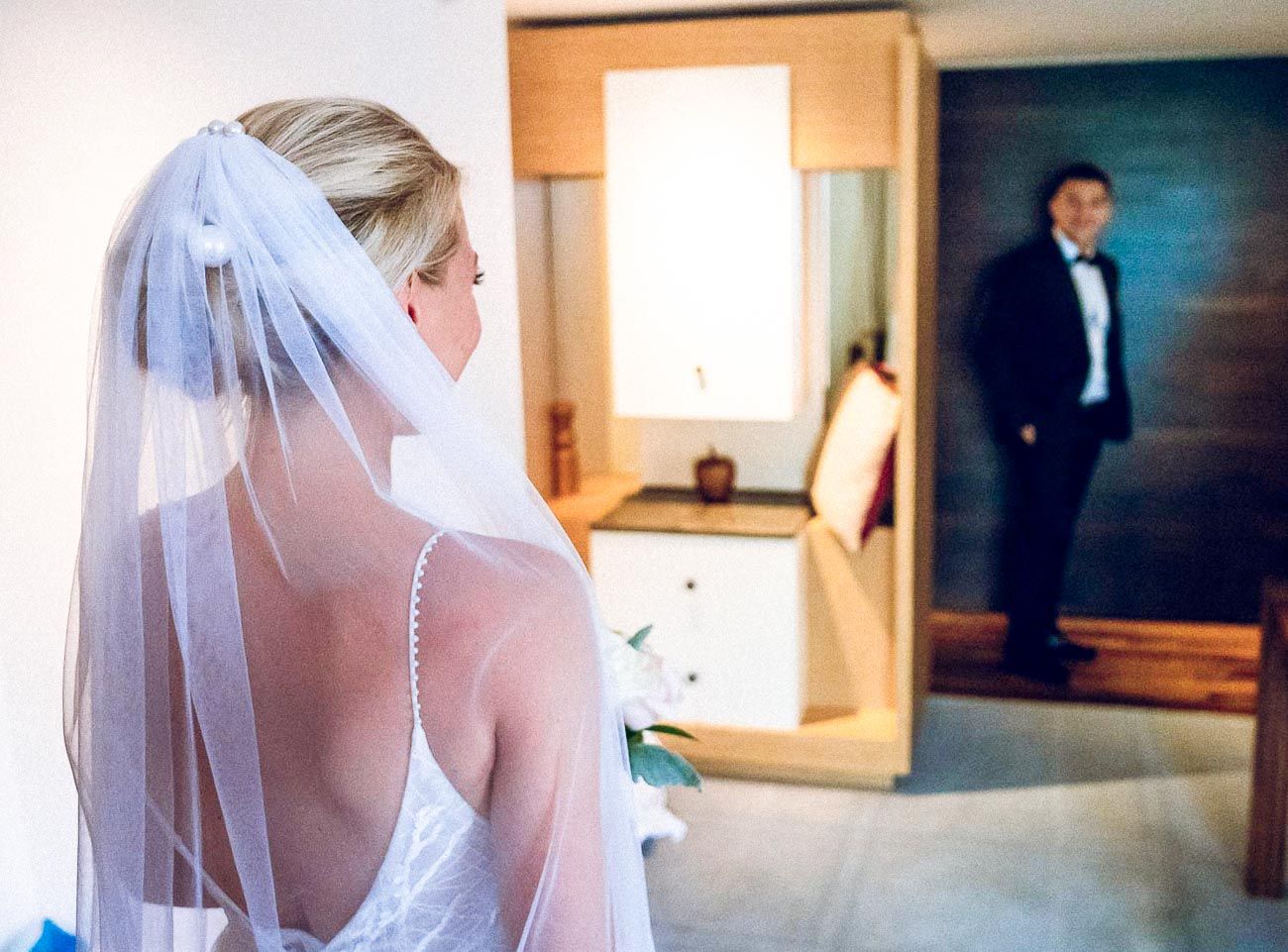 Bride in white wedding dress and veil seeing groom in tuxedo for first look moment.