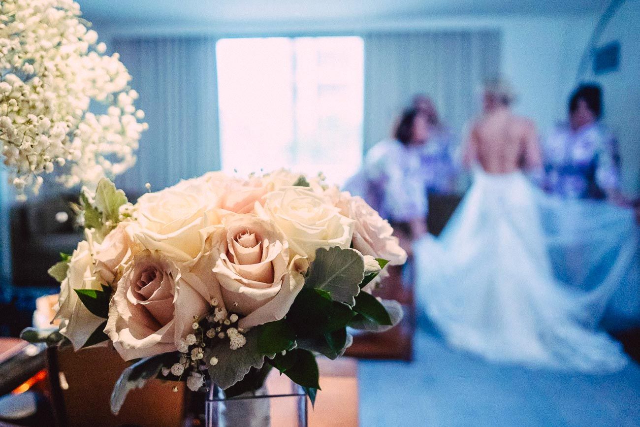 Blush rose bridal bouquet in foreground with bride being dressed in background.
