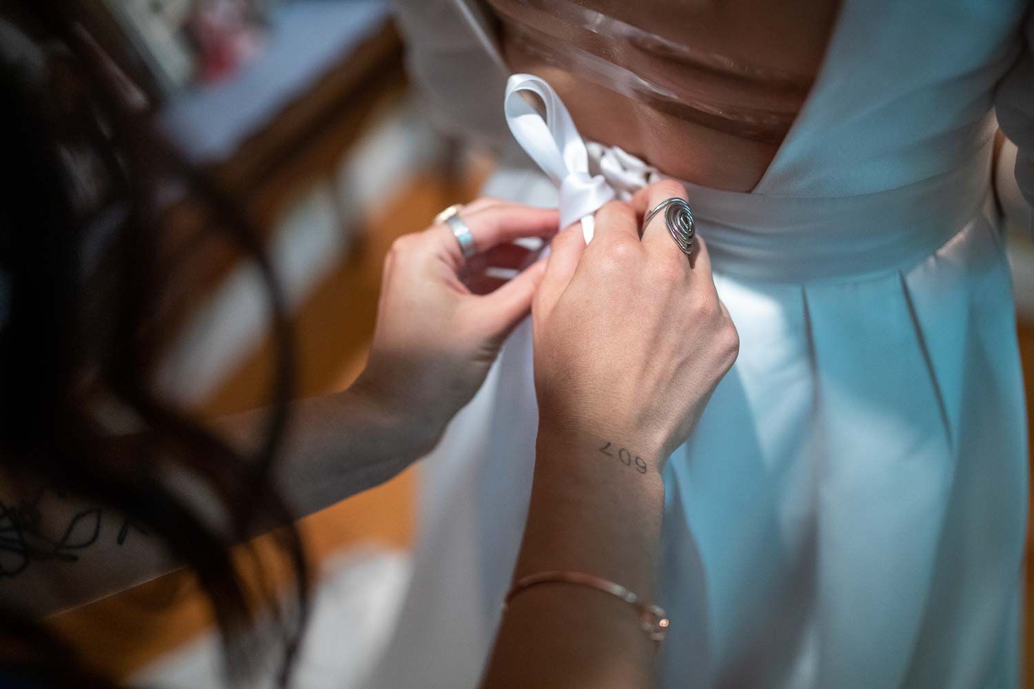 Close-up of bridesmaid carefully lacing and tying back of bride's light blue wedding dress.