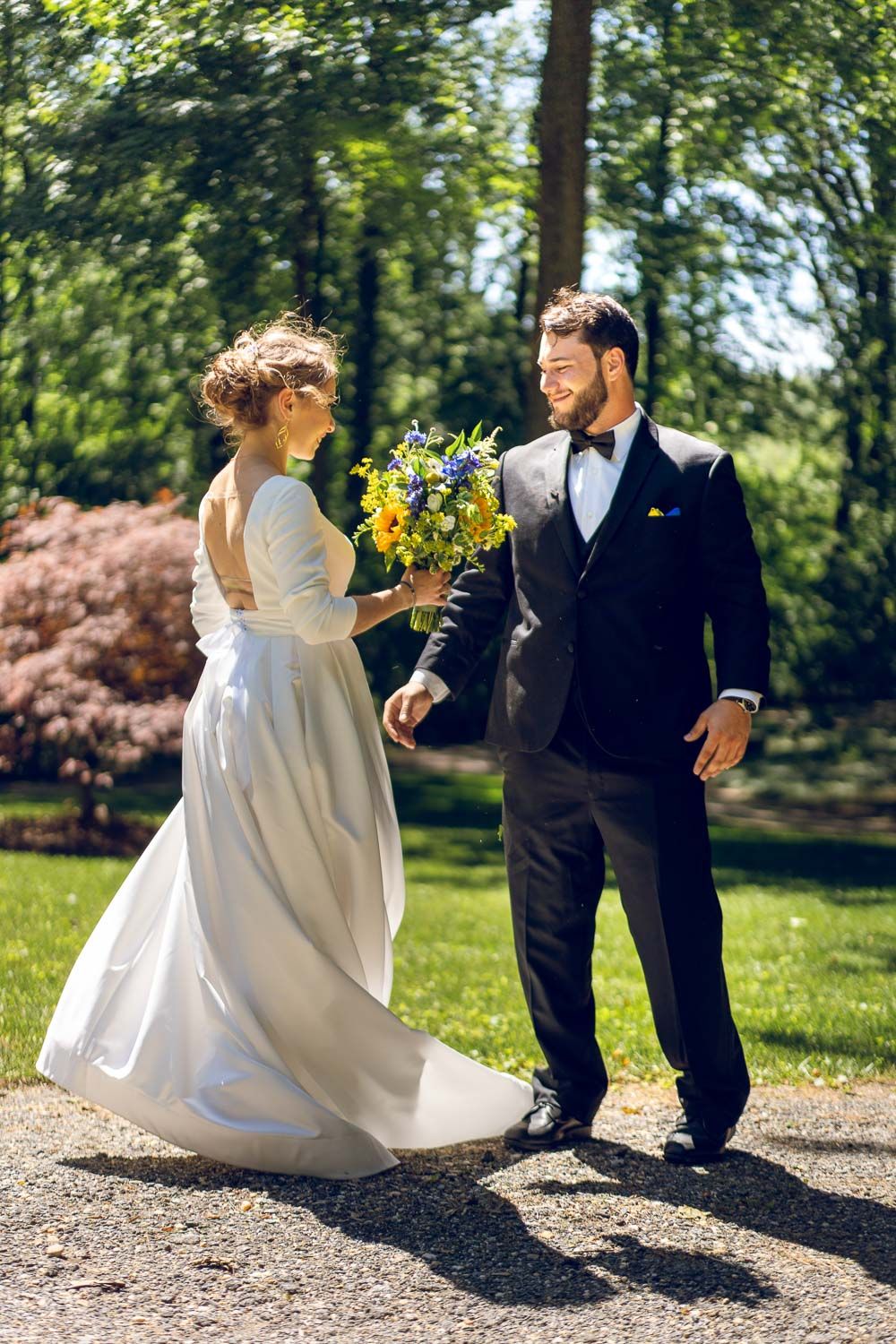 Happy bride and groom walk together in sunlit garden, bride holding vibrant wildflower bouquet.