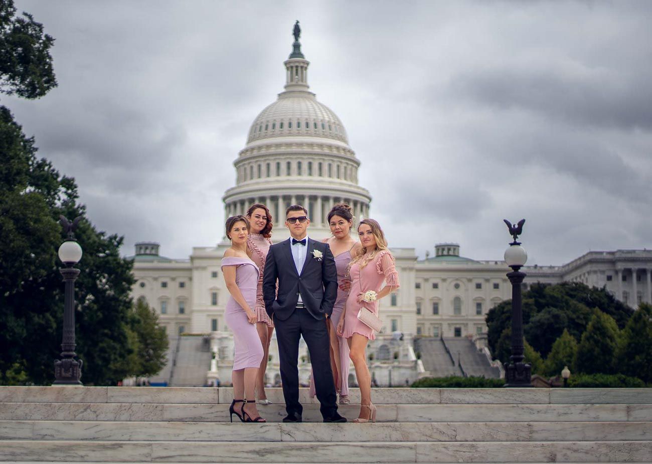 Groom and four bridesmaids in pink dresses pose on steps of US Capitol building.