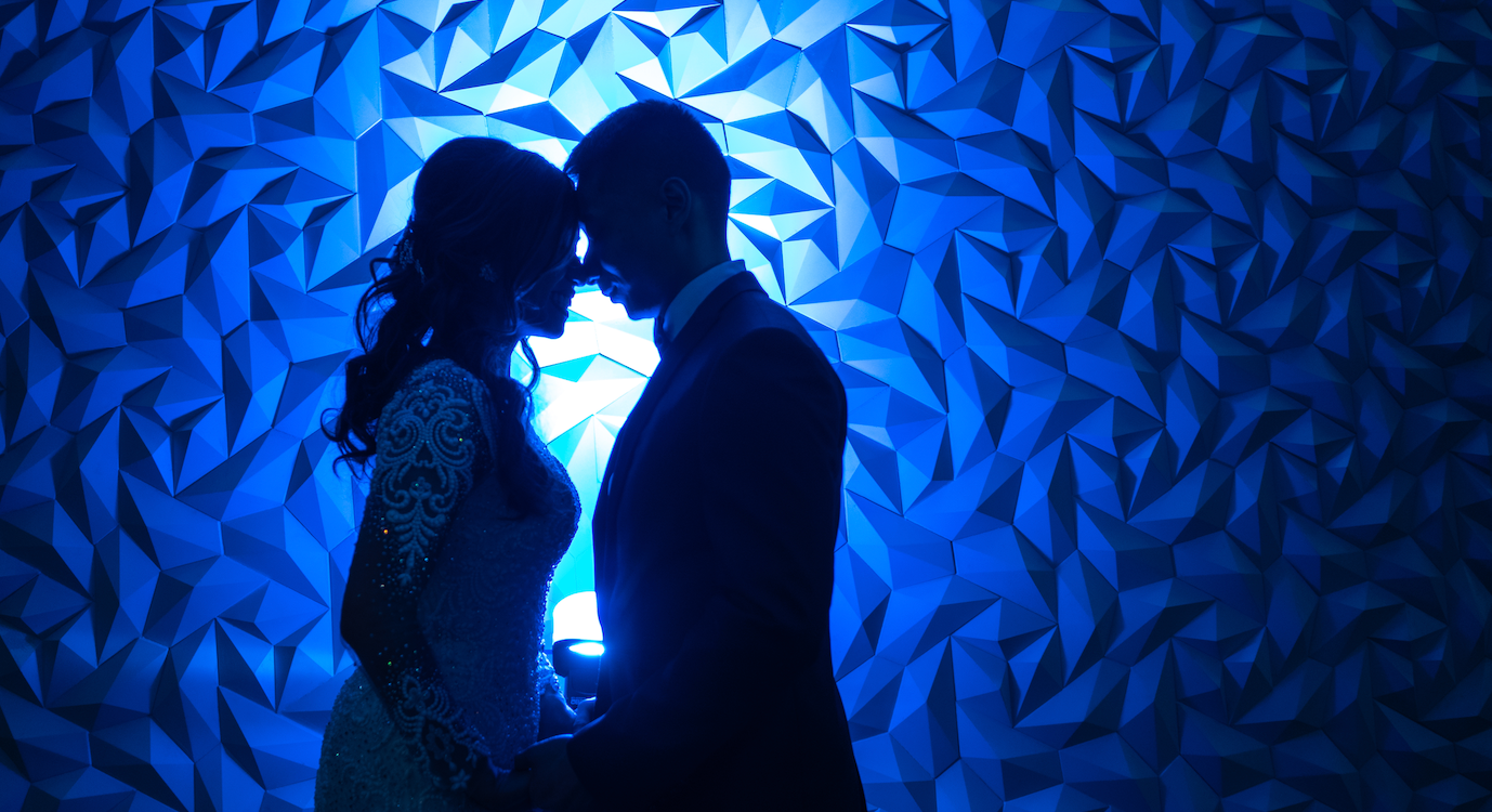 Romantic silhouette of a wedding couple sharing an intimate moment against a blue geometric wall.