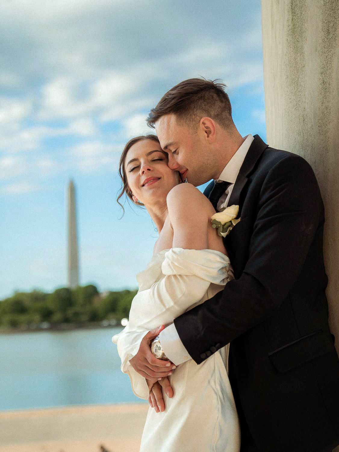 Groom kisses bride on the cheek as she smiles with the Washington Monument visible behind them.