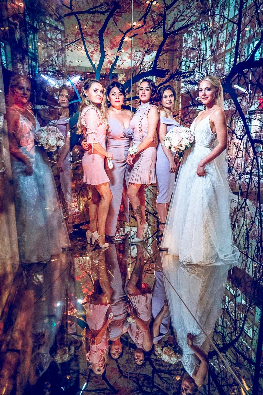 Bride with bridesmaids in pink dresses posing in stunning mirrored room with floral tree decor.