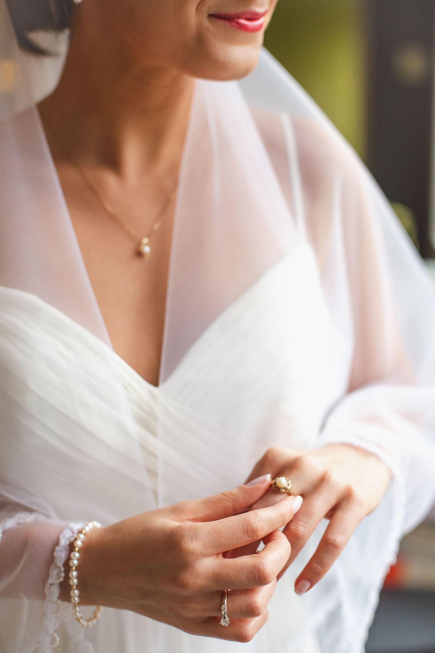 Close-up of bride in white lace gown adjusting ring, wearing pearl bracelet and diamond necklace.
