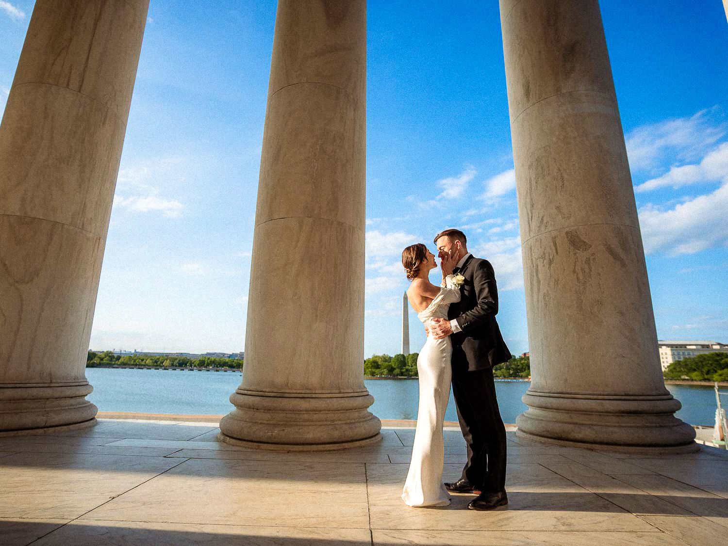 Wedding couple shares a romantic kiss between marble columns at Jefferson Memorial overlooking the Tidal Basin.