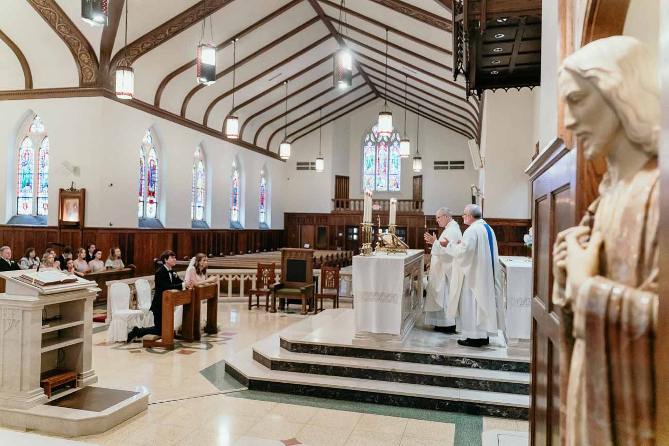 Wide view of a Catholic church wedding Mass with priest at altar and statue of Mary in foreground.