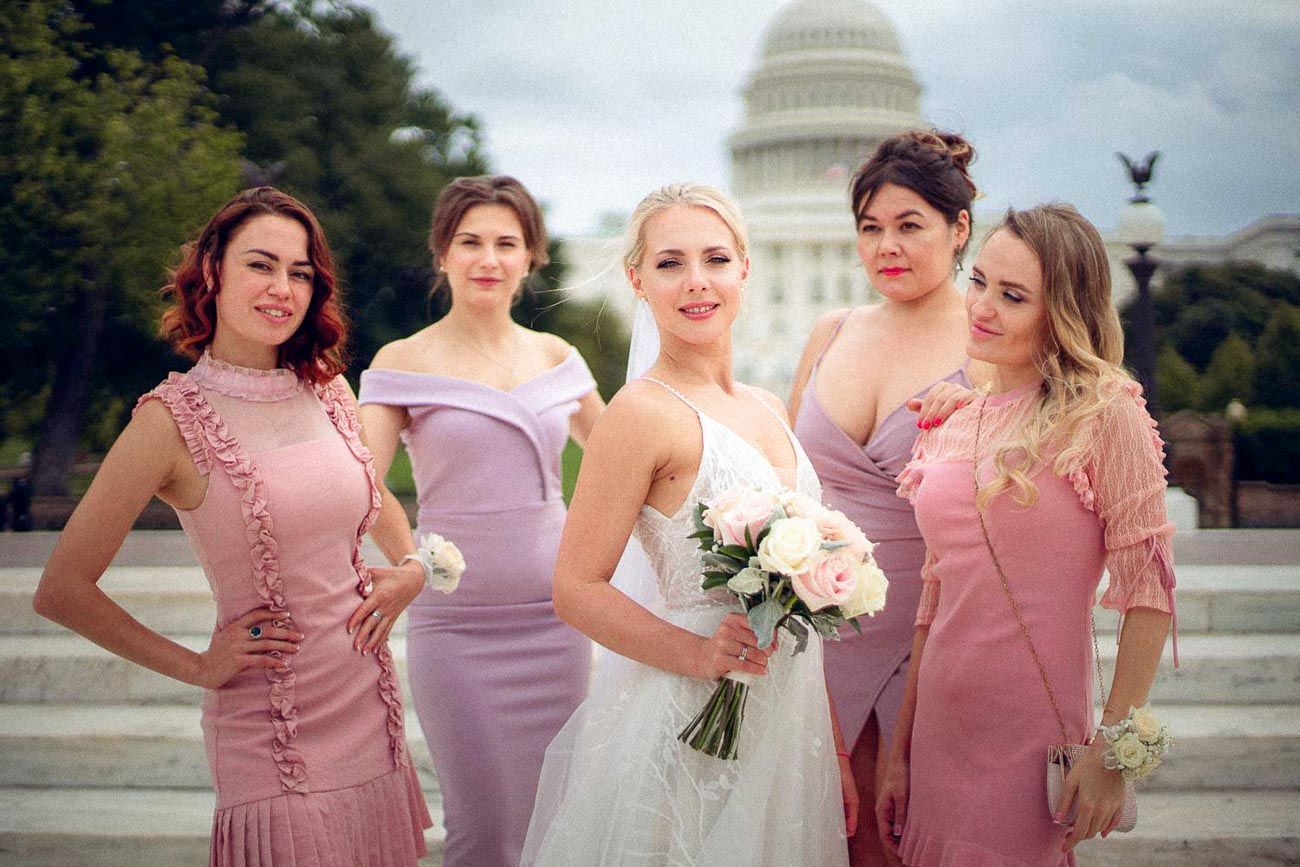 Bride with bouquet and four bridesmaids in pink dresses posing outdoors near US Capitol building.