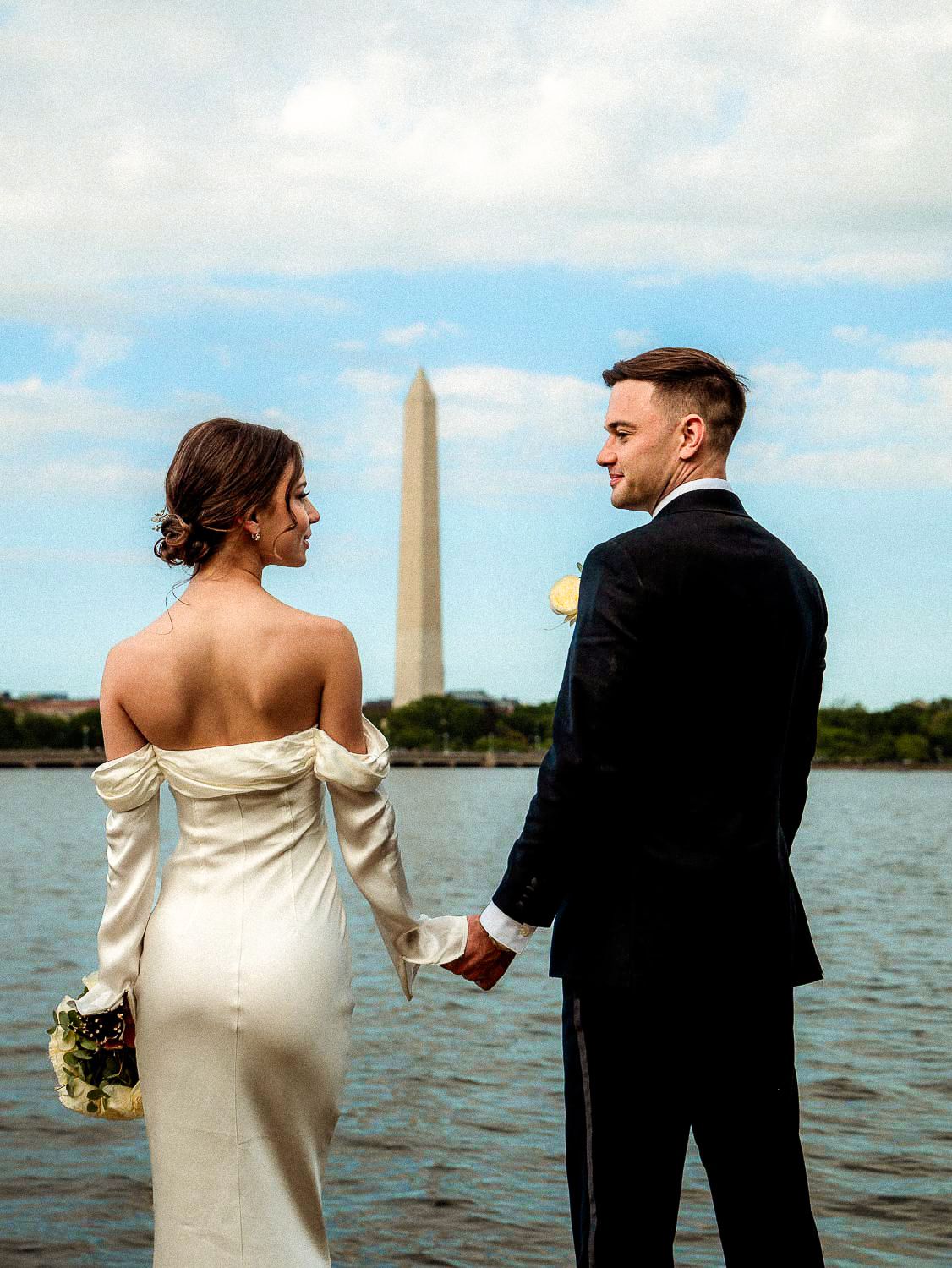 Bride and groom holding hands facing the Washington Monument across the Tidal Basin.