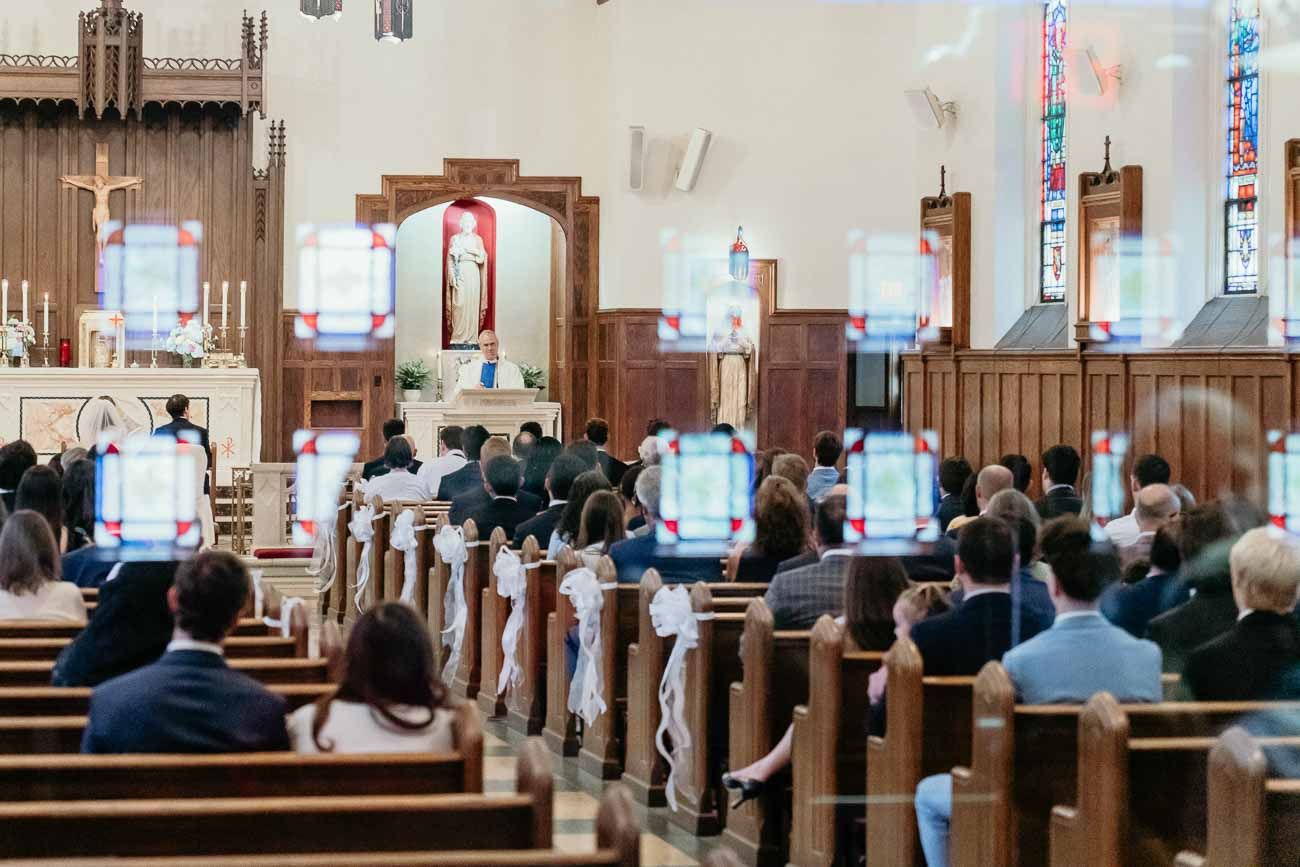 Guests seated in wooden pews during a Catholic wedding ceremony in a decorated church.
