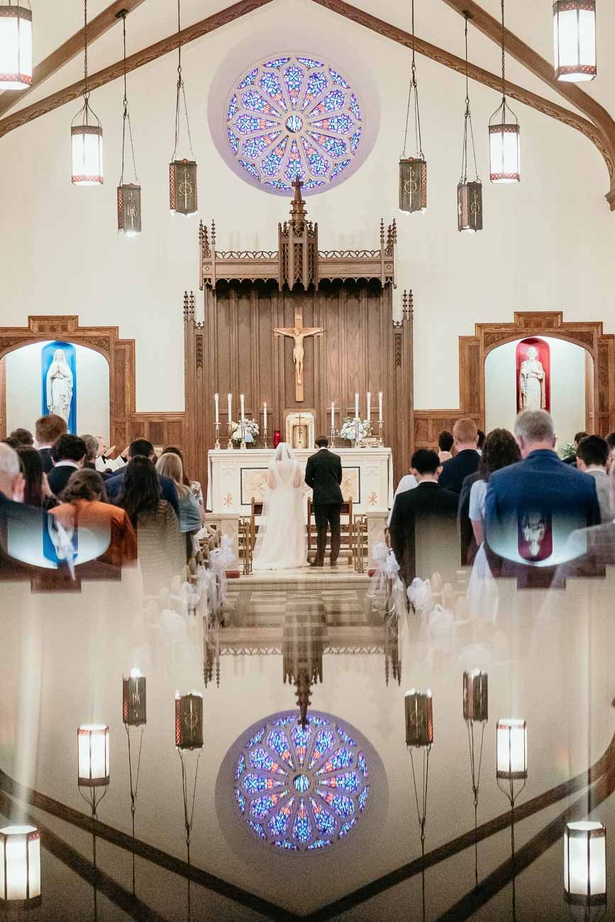 Wedding ceremony inside a beautiful Catholic church with a stunning rose window above the altar.