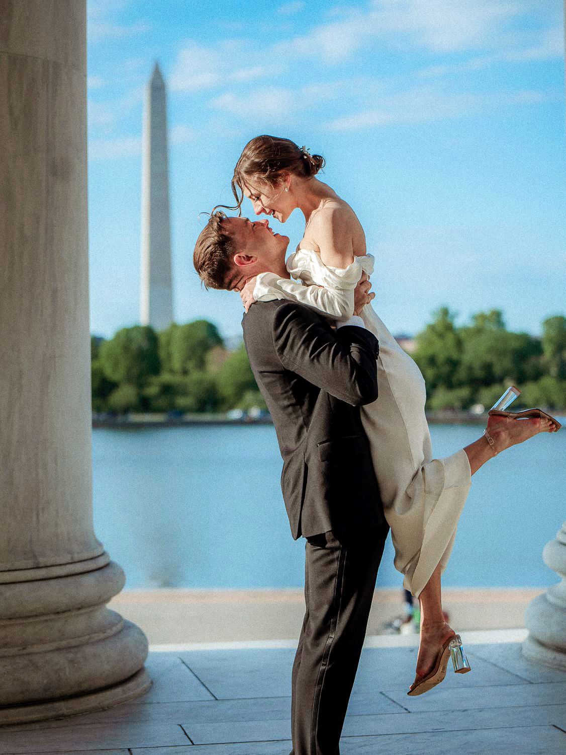Bride lifted by groom at Jefferson Memorial with Washington Monument backdrop.
