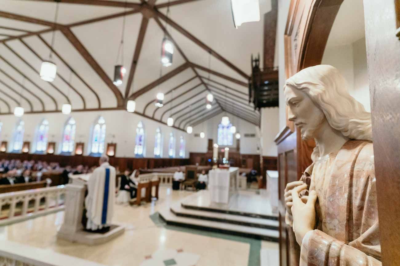 Wide-angle view of a Catholic church interior with a religious statue in the foreground during a wedding.