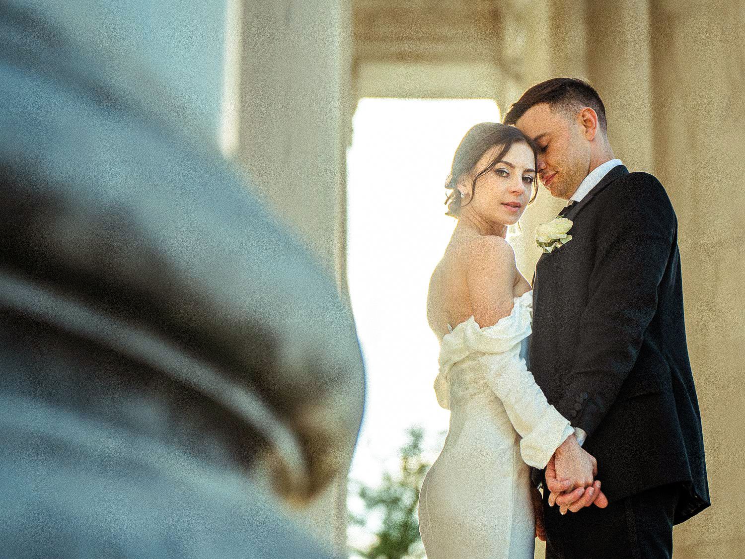 Elegant bride and groom hold hands intimately between marble columns at the Jefferson Memorial.
