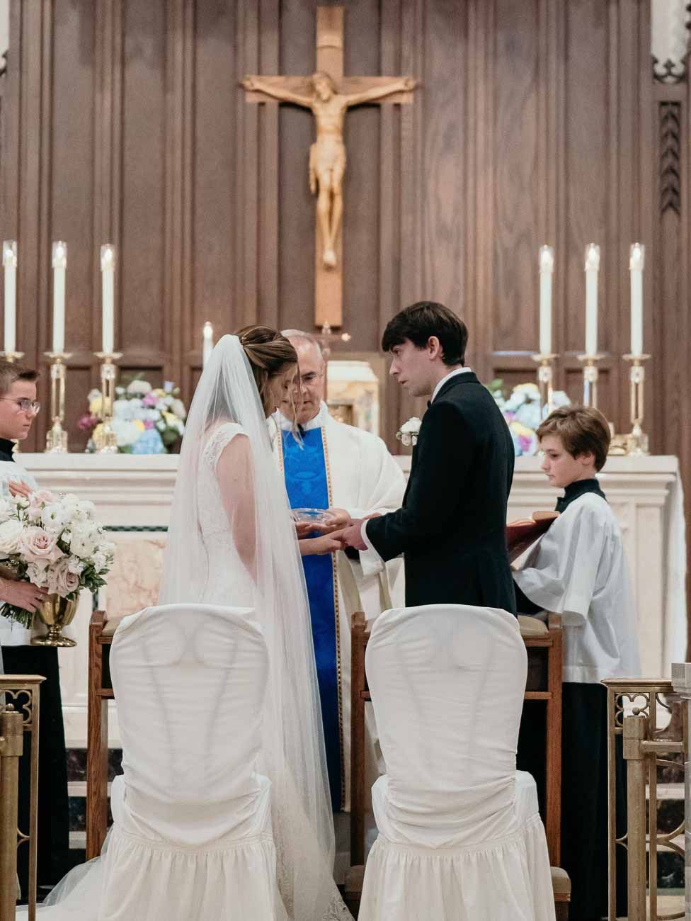 Bride and groom exchange vows before a priest in a candlelit Catholic church ceremony.