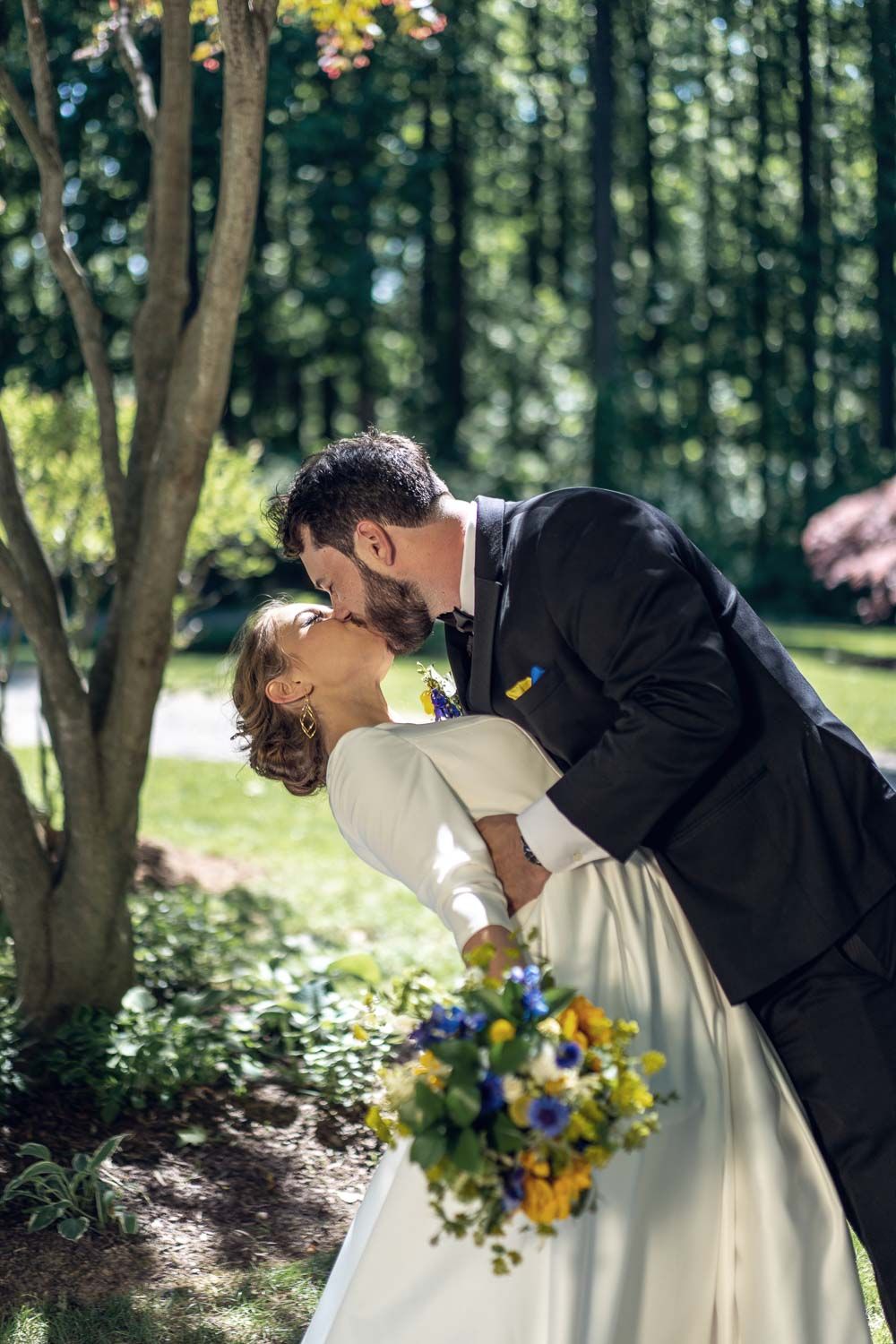 Groom dipping bride for romantic kiss while she holds vibrant yellow and blue bouquet.