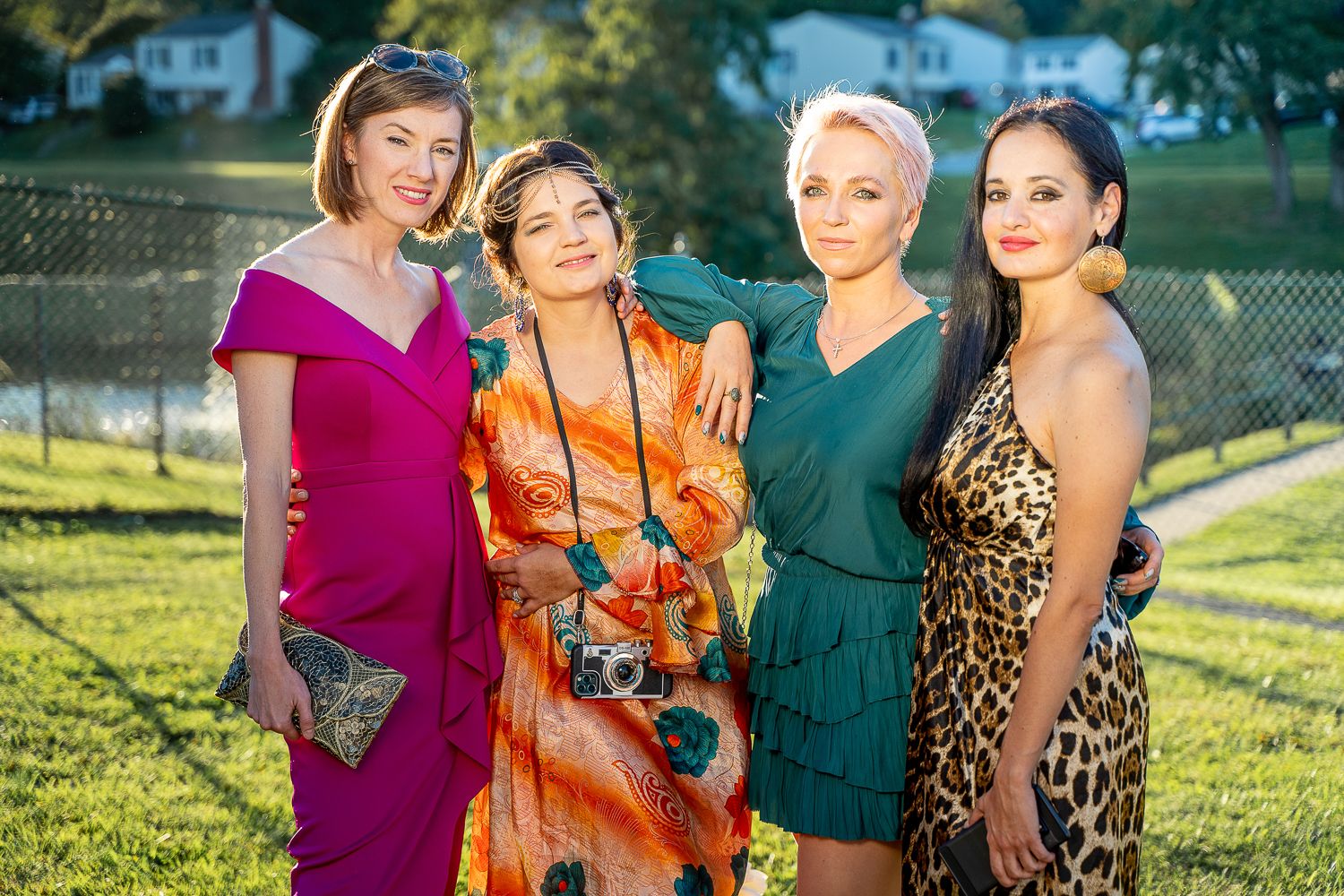 Four elegantly dressed women posing together outdoors at a garden event in colorful formal attire.