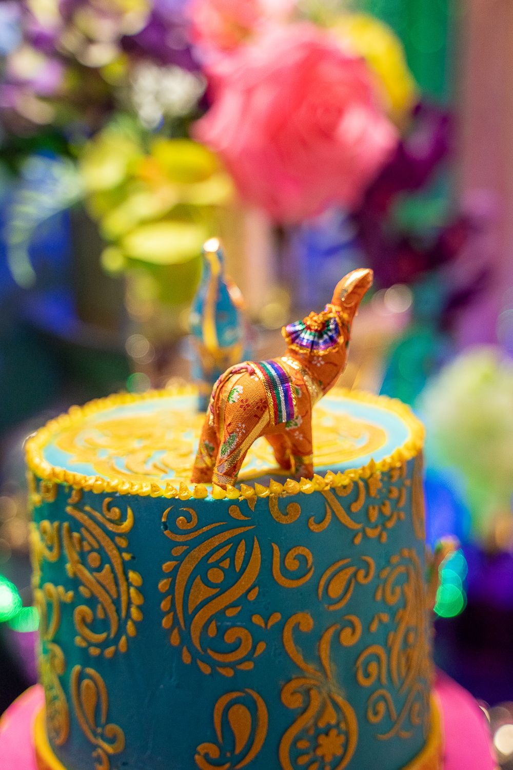 Teal and gold paisley-decorated birthday cake topped with a colorful ornate camel figurine.