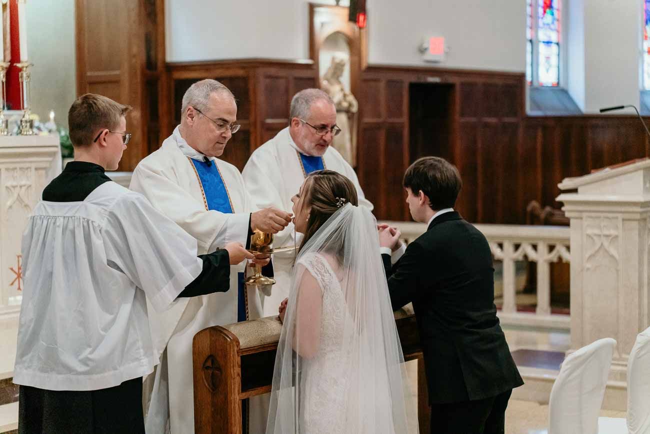 Priest places wedding ring on brides finger during a traditional Catholic wedding ceremony at the altar.