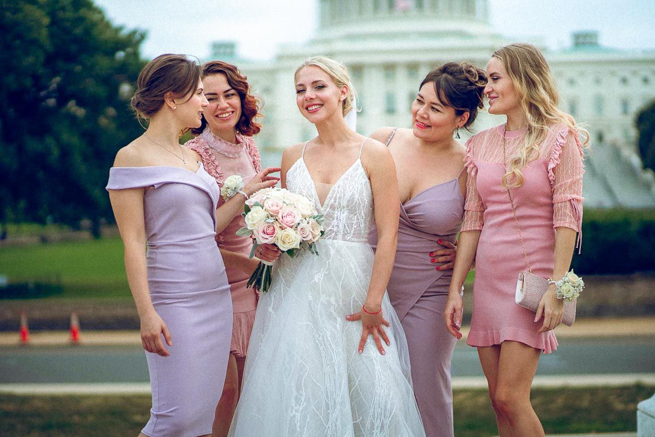 Smiling bride with bouquet surrounded by four bridesmaids in mauve dresses at the US Capitol.