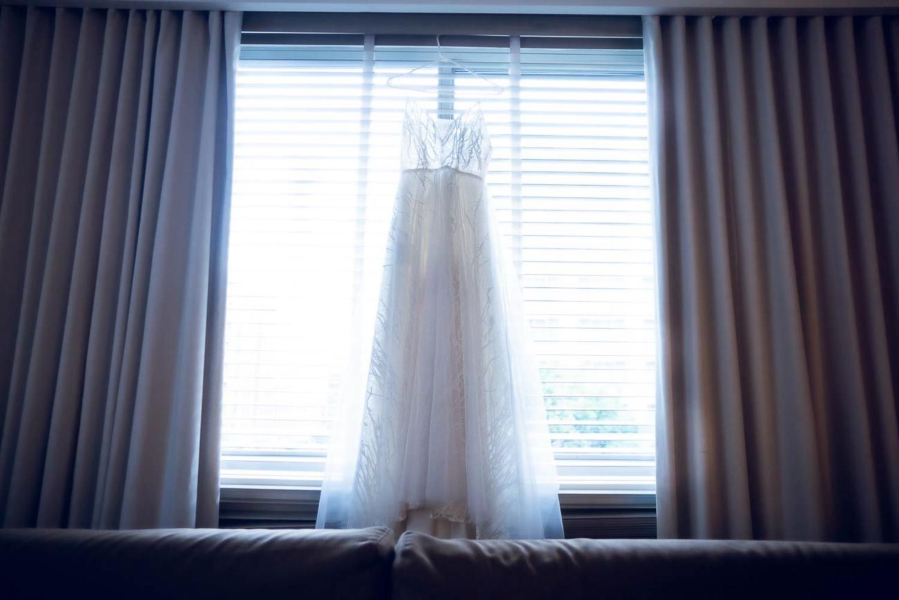Elegant white wedding dress hanging in window with soft natural light.