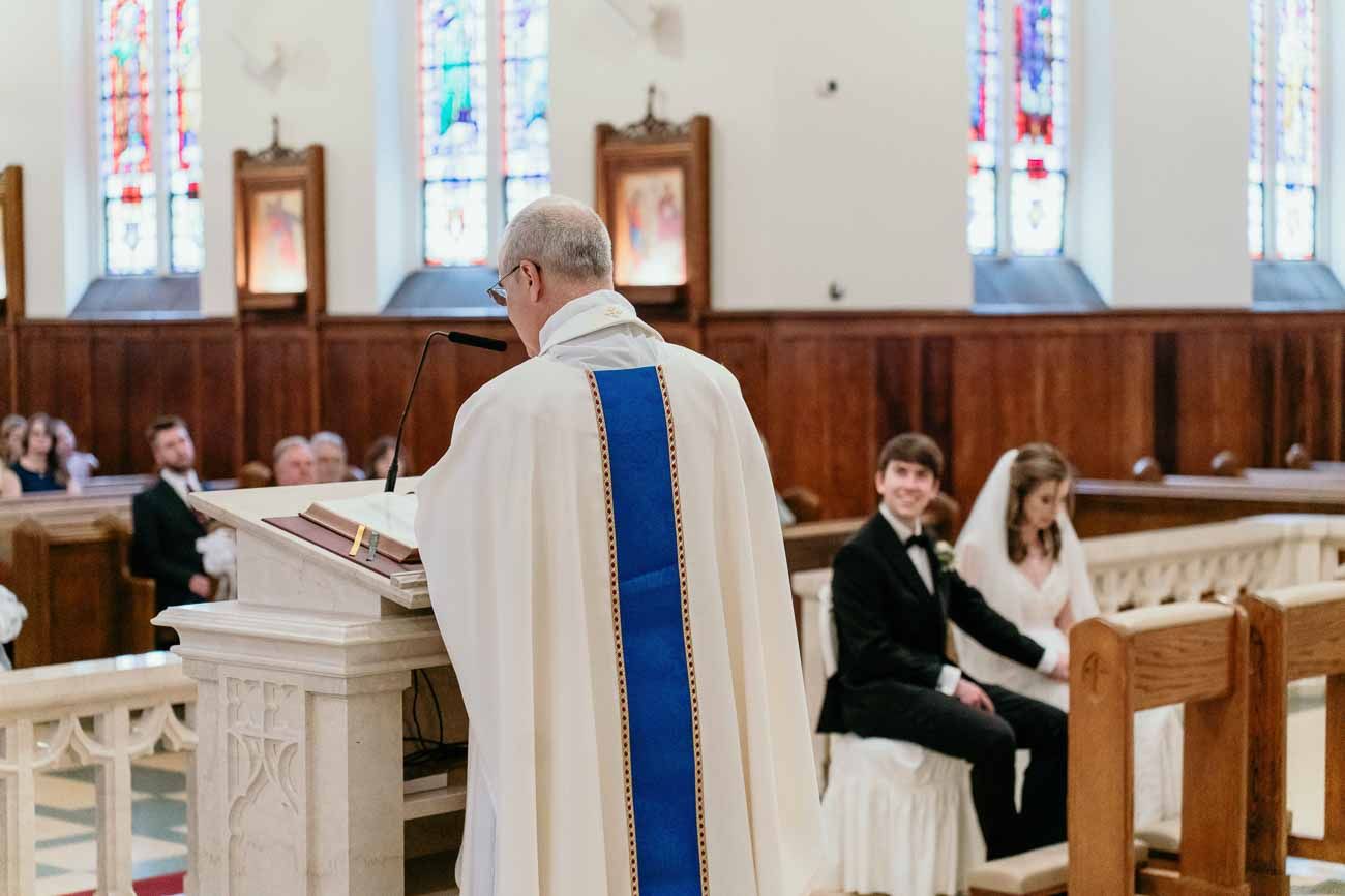Catholic priest in white vestments officiating a wedding ceremony at the altar pulpit.