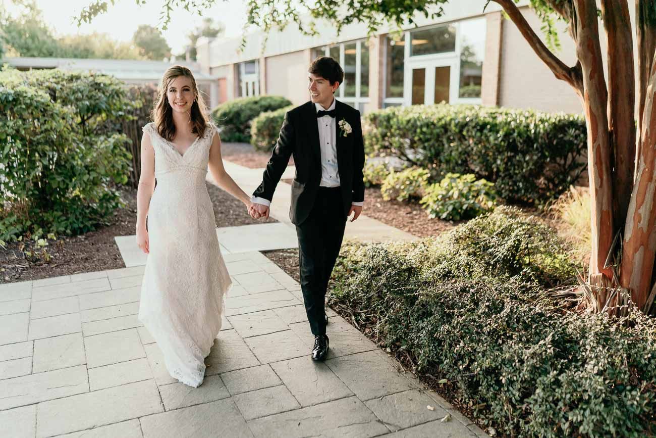 Bride and groom walk hand in hand along a garden pathway on their wedding day.