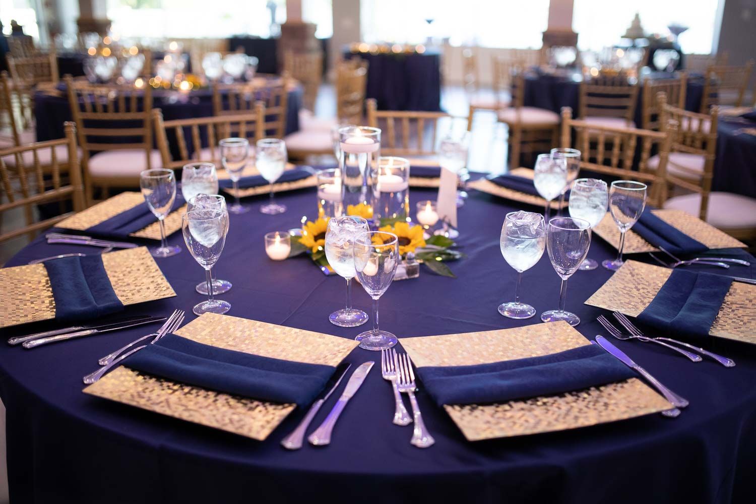 Elegant navy and gold wedding reception table with sequin chargers, crystal glasses, and floral centerpiece.